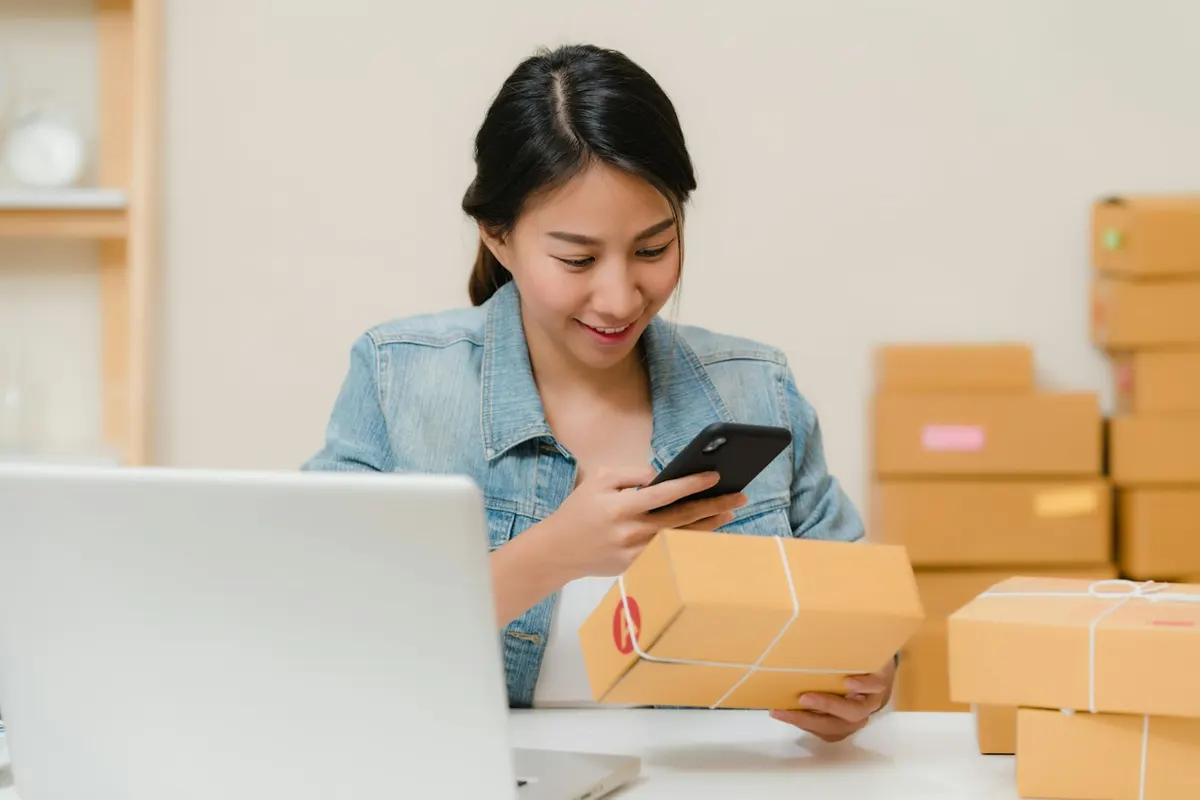 Una ragazza prepara un ordine con il telefono e il portatile